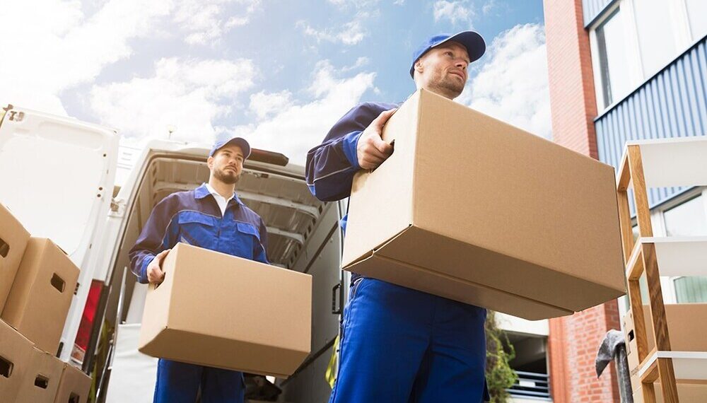 Close-up Of Two Delivery Men Carrying Cardboard Box